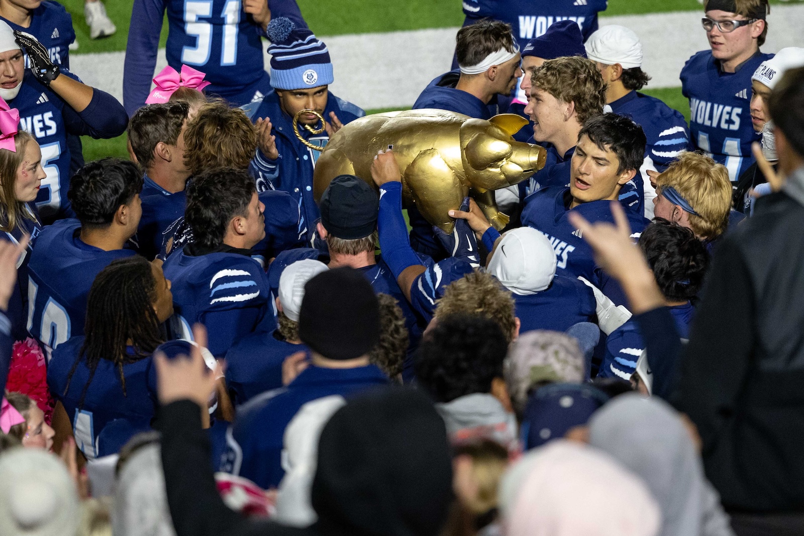 CHS-WPHS-FB-49 | Press Pass Sports Blue-clad football players surround and celebrate around a large shiny gold pig trophy on the field in a crowded huddle.
