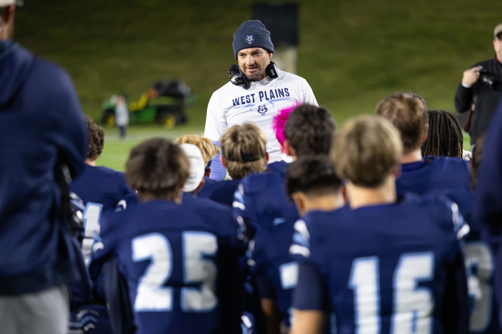 CHS-WPHS-FB-50 | Press Pass Sports Coach wearing a navy beanie and headset talks to a football team in blue jerseys on the field, West Plains emblazoned on his shirt.