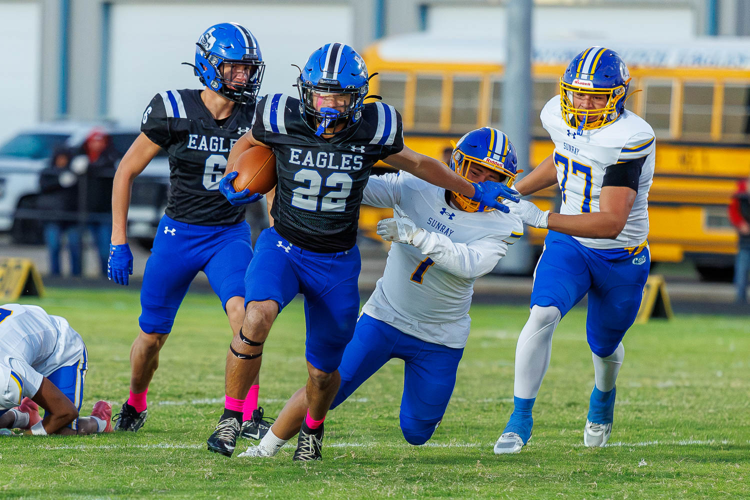 _P7A1234 | Press Pass Sports Football game action: a black Eagles jersey runner (#22) dashes with the ball as teammates shield him, while a Sunray defender in white reaches in from the right to tackle; another Sunray player watches nearby on a grassy field.