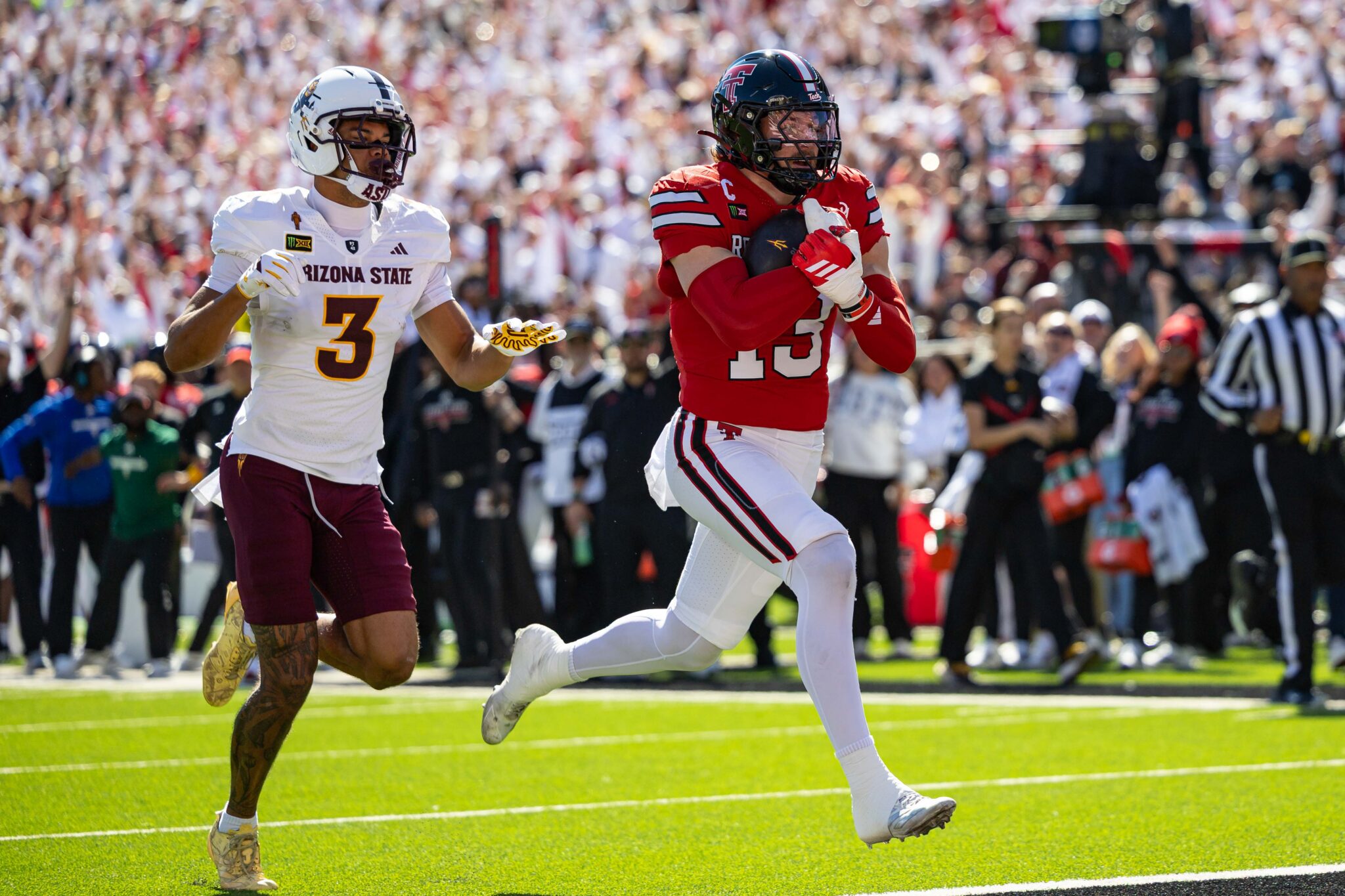 Arizona State University player wearing white #3 chases a red-team ball carrier down the field as a crowded stadium watches.