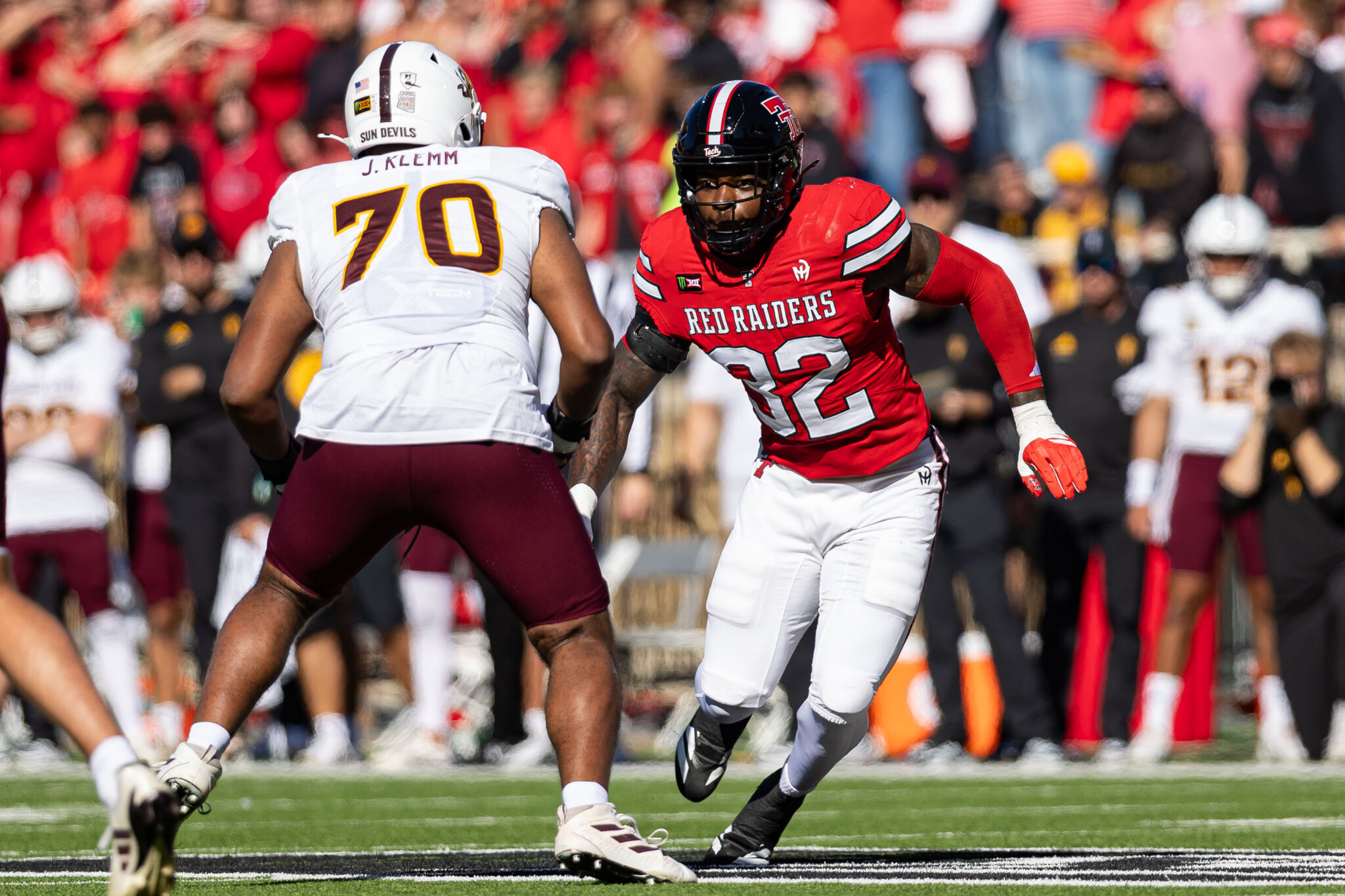 Two football players in a crowded stadium engage in a play: a White-era defender (J. Klemm, #70) facing a Red Raiders runner in red jersey.
