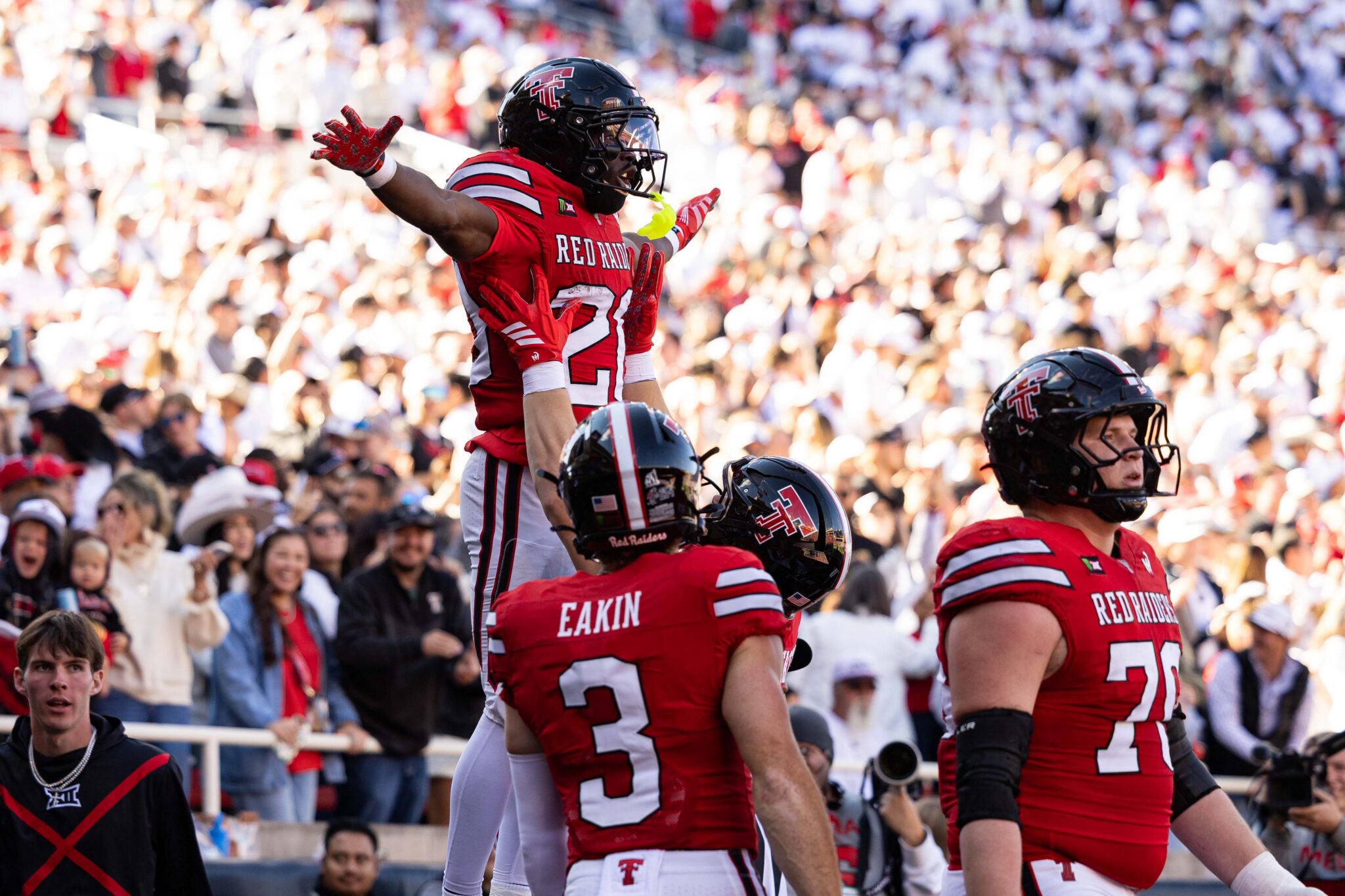 Football players in red uniforms celebrate a touchdown as the stands erupt with cheering fans behind them.