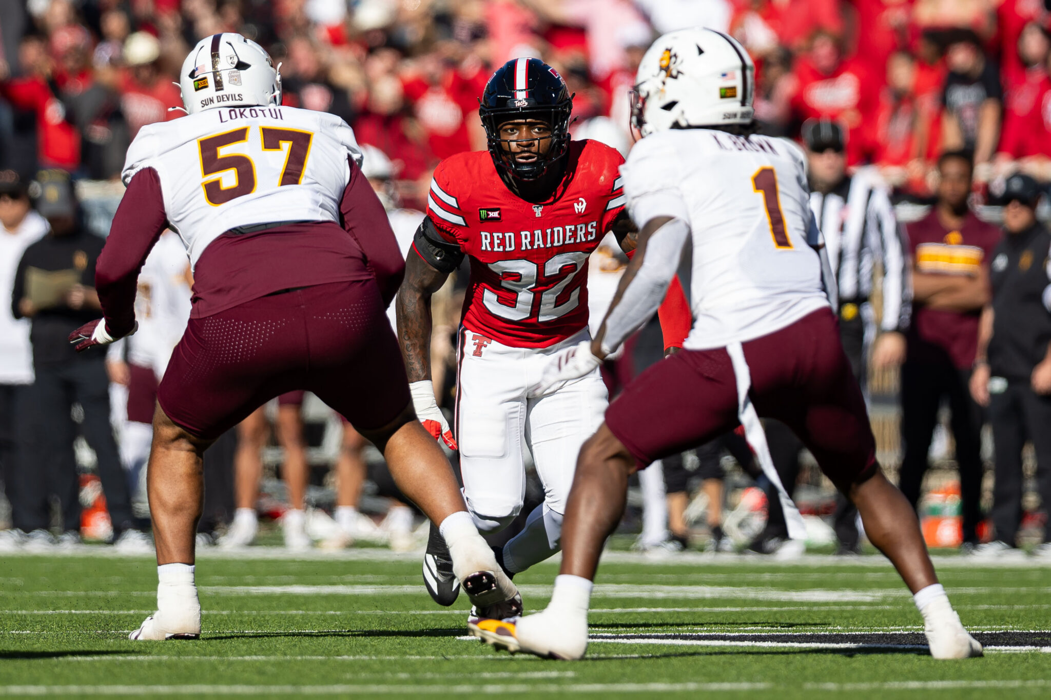 Red Raiders player #32 runs with the ball, surrounded by defenders in white jerseys on a football field.