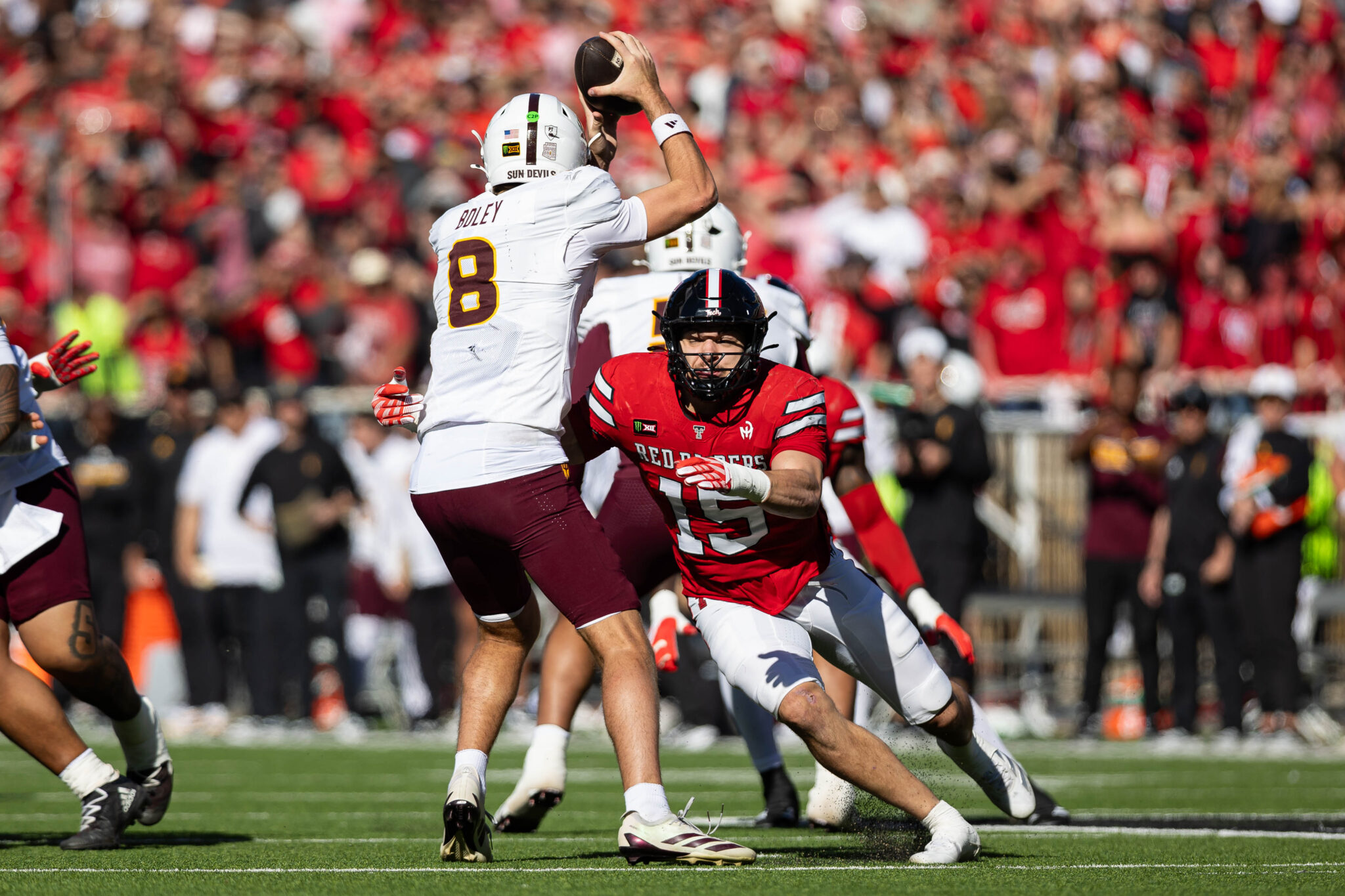 Quarterback in white and maroon jersey #8 leaps to catch a pass as defenders in red close in, on a crowded stadium field. (Informative)
