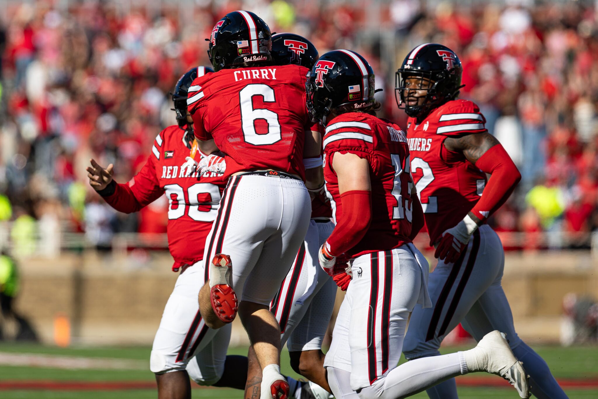 Texas Tech Red Raiders football players celebrate on the field in red uniforms against a blurred crowd background.