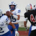 1K6A3376 | Press Pass Sports Quarterback in a Stratford white-and-blue uniform grips a football, looking to pass during a football game on a track field.