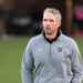 20261015-Dumas-Randall-FB-001 | Press Pass Sports Man wearing a gray Raiders jacket stands on a grassy field, looking off to the right with a neutral expression.