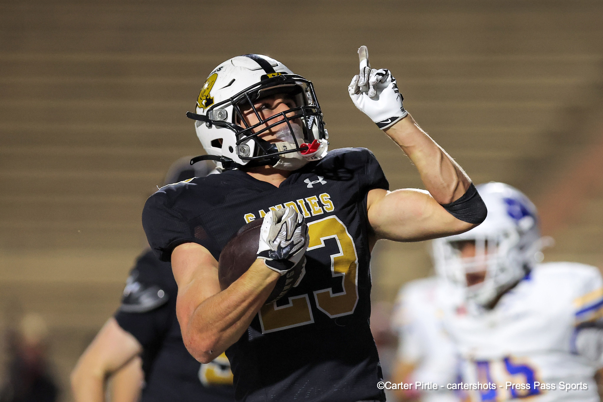 Football player in a black uniform raises one finger in celebration on the field, holding the ball.