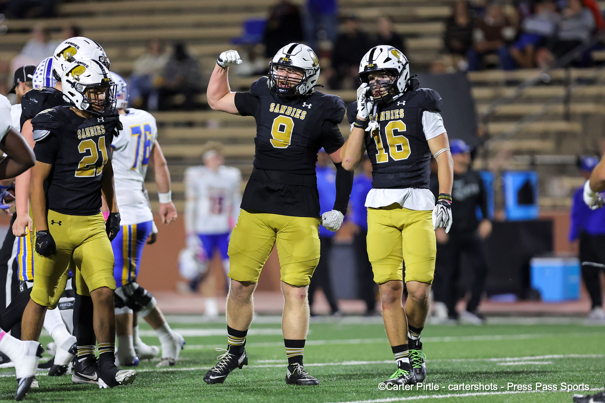 Football players from the Sandies celebrate on the field after a play, wearing black jerseys with gold numbers and white helmets.