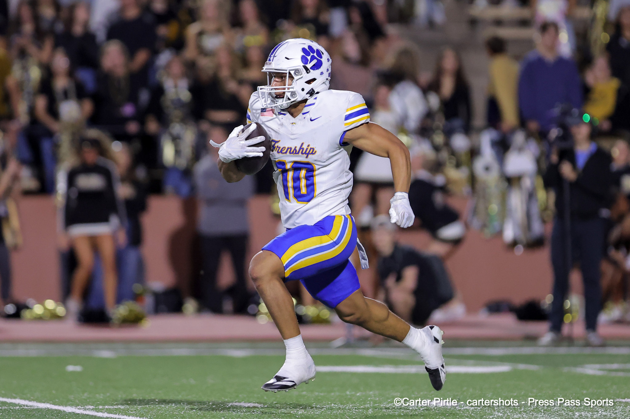 Football player in a white, purple, and yellow uniform runs with the ball on a green field, crowd in the stands behind him.