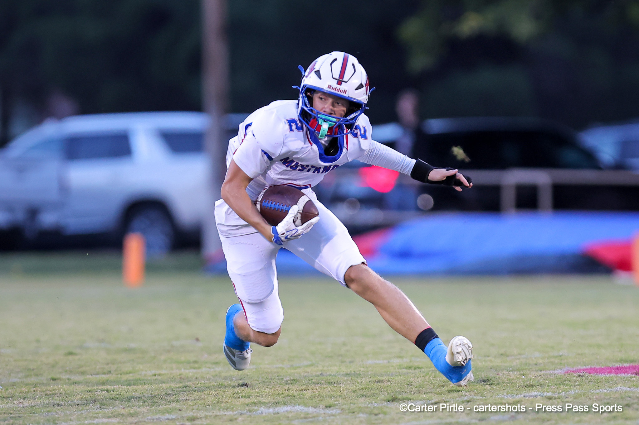 Football player in a white uniform and helmet carrying the ball while sprinting on a grassy field during a game.