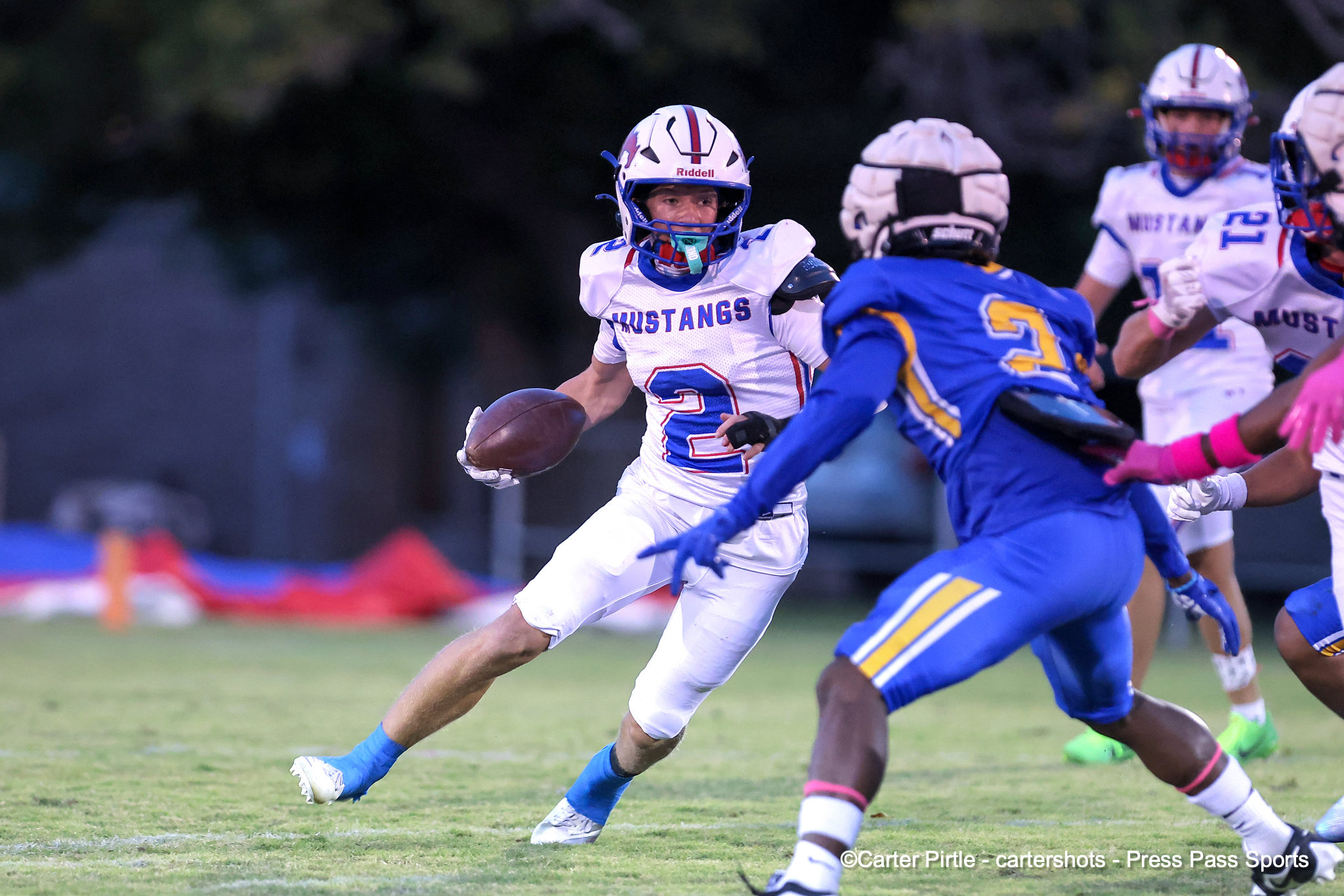 Football player from the Mustangs carrying the ball, sprinting past defenders on a grass field during a game.