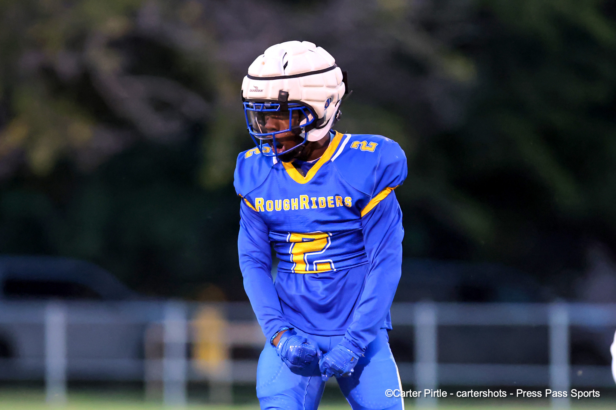 Football player in a blue and yellow RoughRiders uniform, wearing a white helmet with a blue face mask on the field.