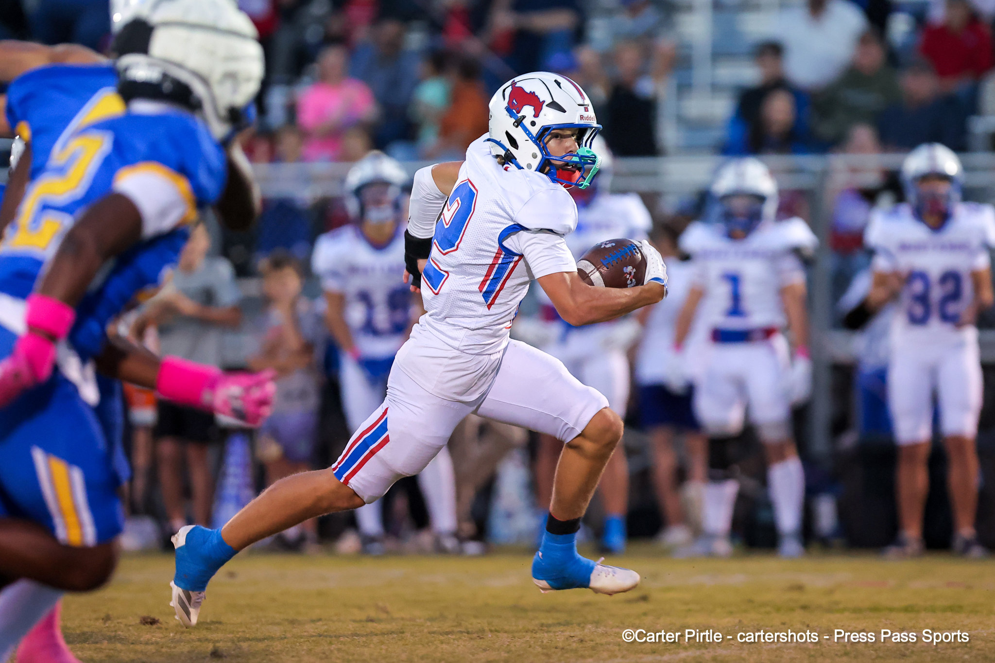 Football player in a white uniform runs with the ball during a game, with a cheering crowd in the stands behind him.