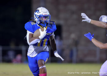 20261023-Claude-BR-FB-021 | Press Pass Sports American football player in blue and yellow jersey runs with the ball, evading a defender reaching in from the right.
