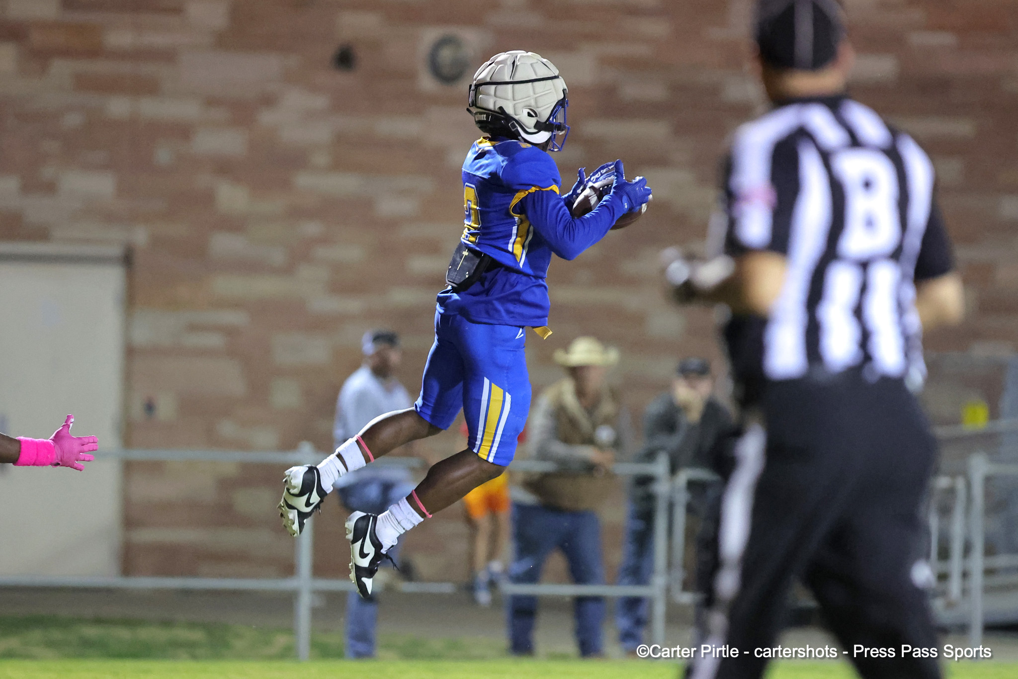 Young football player in blue and yellow uniform jumps in midair, catching a football during a game.