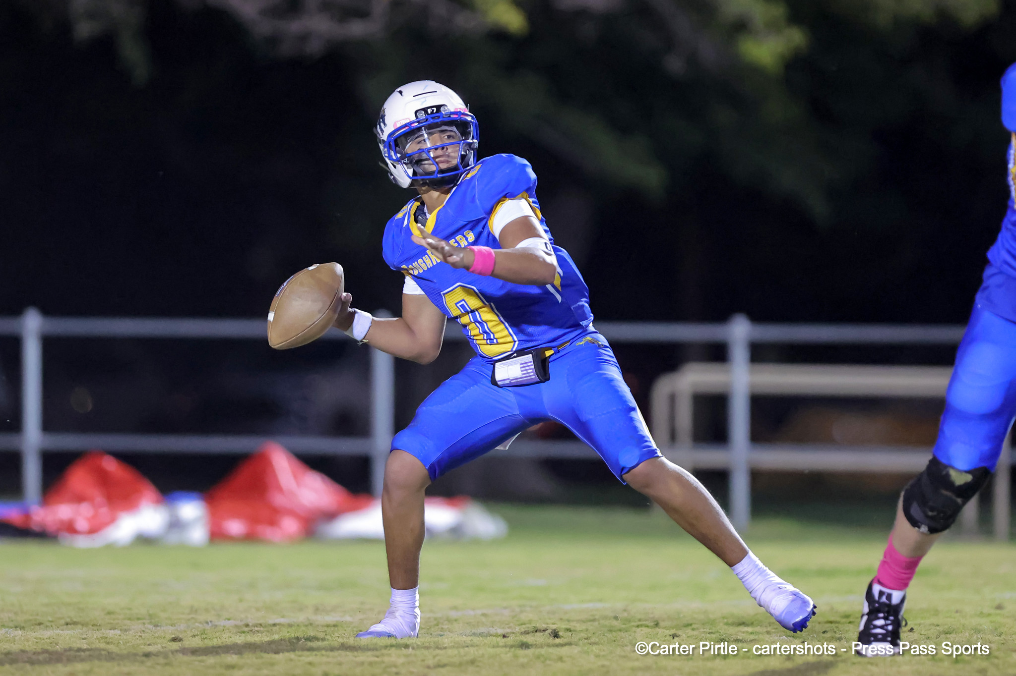 Football player in blue and yellow uniform runs with the ball during a night game, wearing a white helmet with a blue facemask.