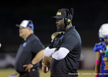 20261023-Claude-BR-FB-027 | Press Pass Sports Coach on the sideline at night wearing a headset and a black cap, arms crossed.