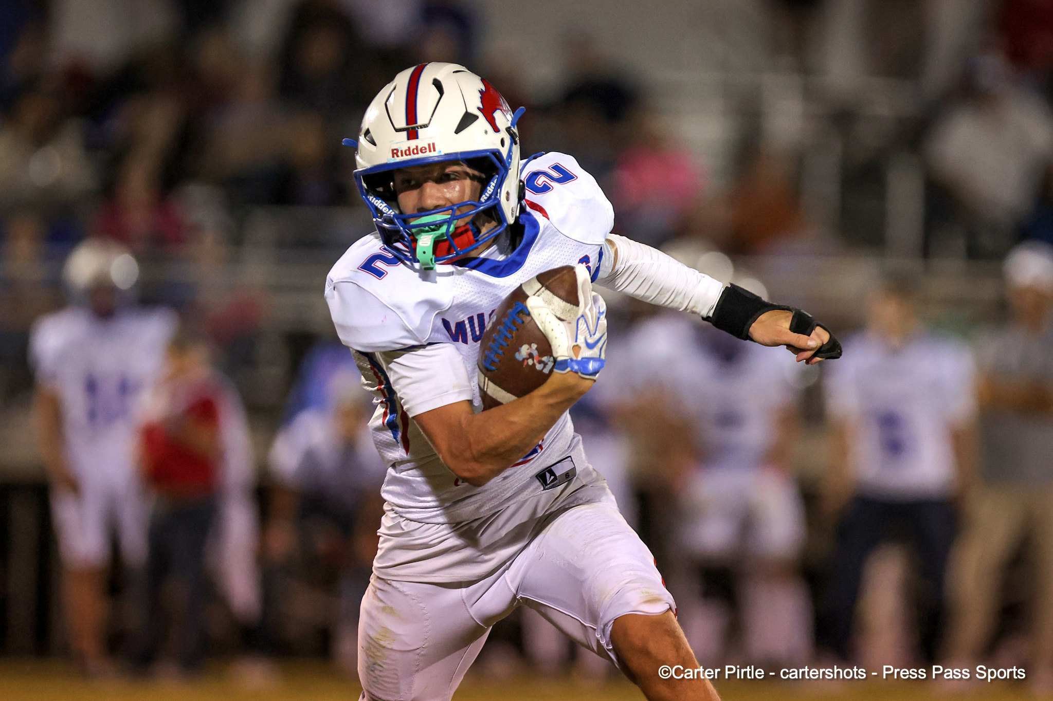 Football player in a white uniform runs with the ball during a game, blurred crowd in the background.