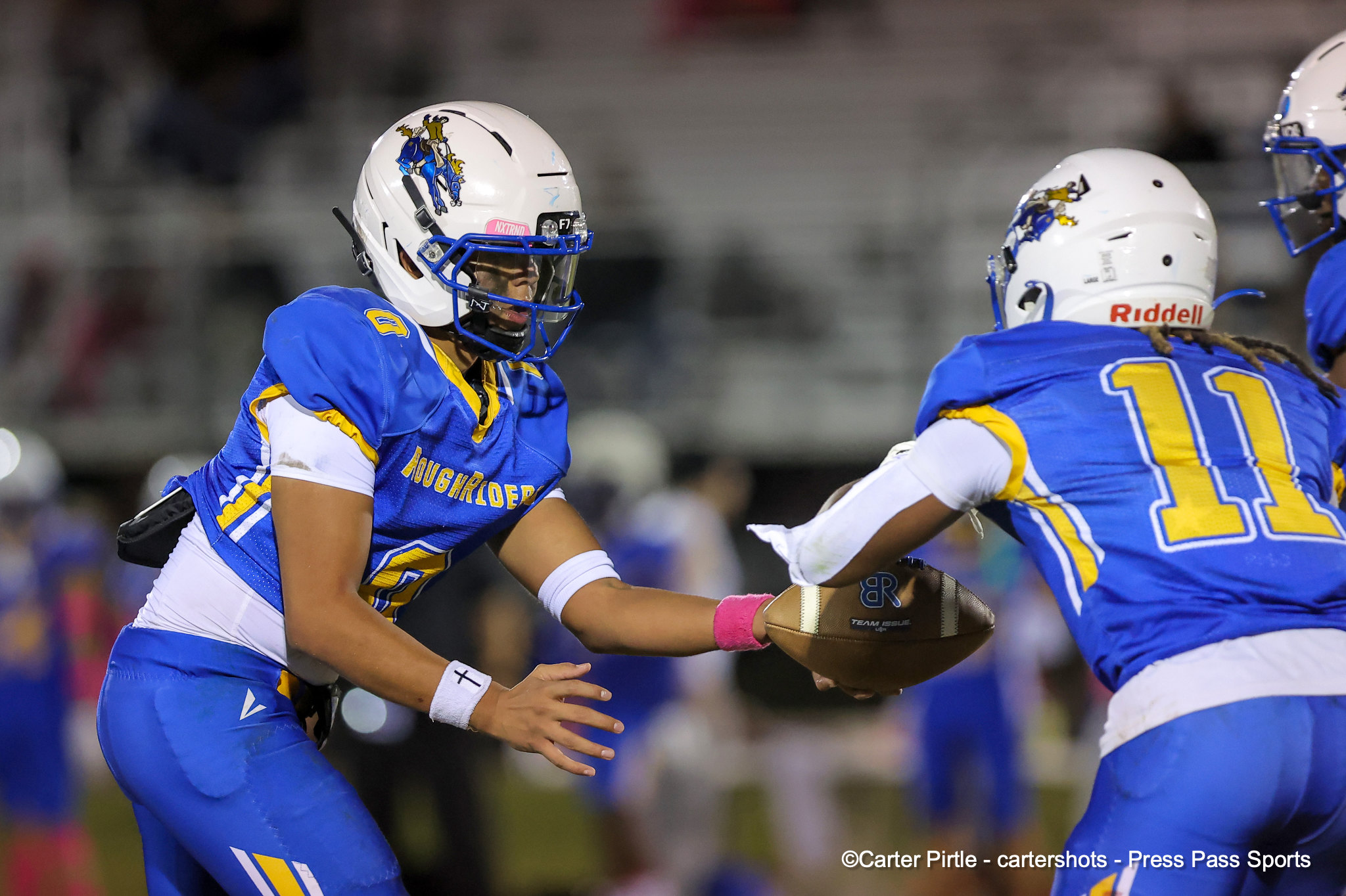 Two football players in blue and yellow uniforms clash on the field during a game, helmets on and eyes focused on the play.
