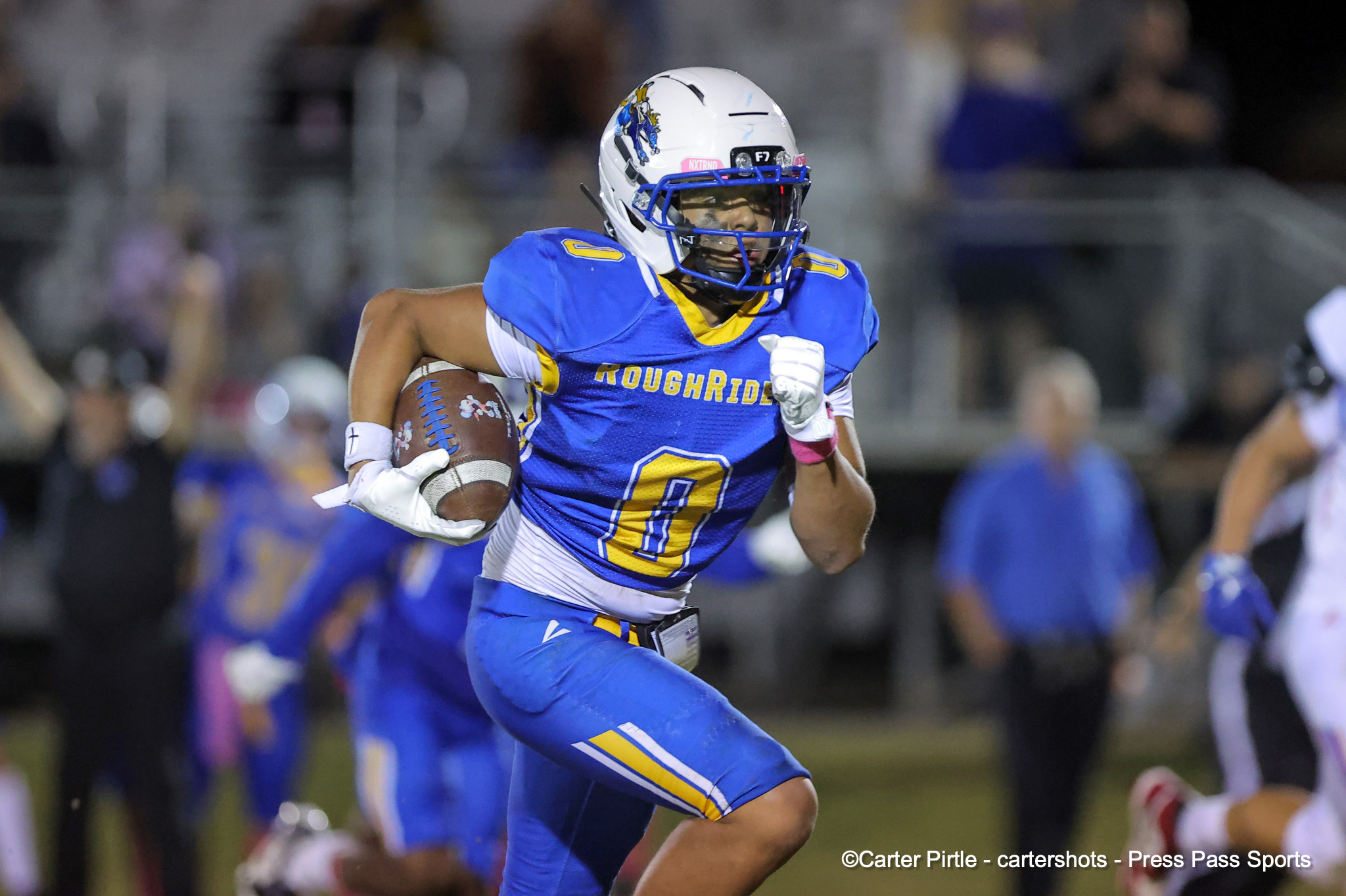 Football player in blue and yellow uniform running with ball during a game in a crowded stadium.