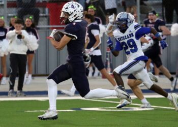 1K6A6612 | Press Pass Sports Navy-clad football player with the ball runs toward the end zone as a blue-and-white defender chases him.