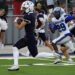 1K6A6612 | Press Pass Sports Navy-clad football player with the ball runs toward the end zone as a blue-and-white defender chases him.