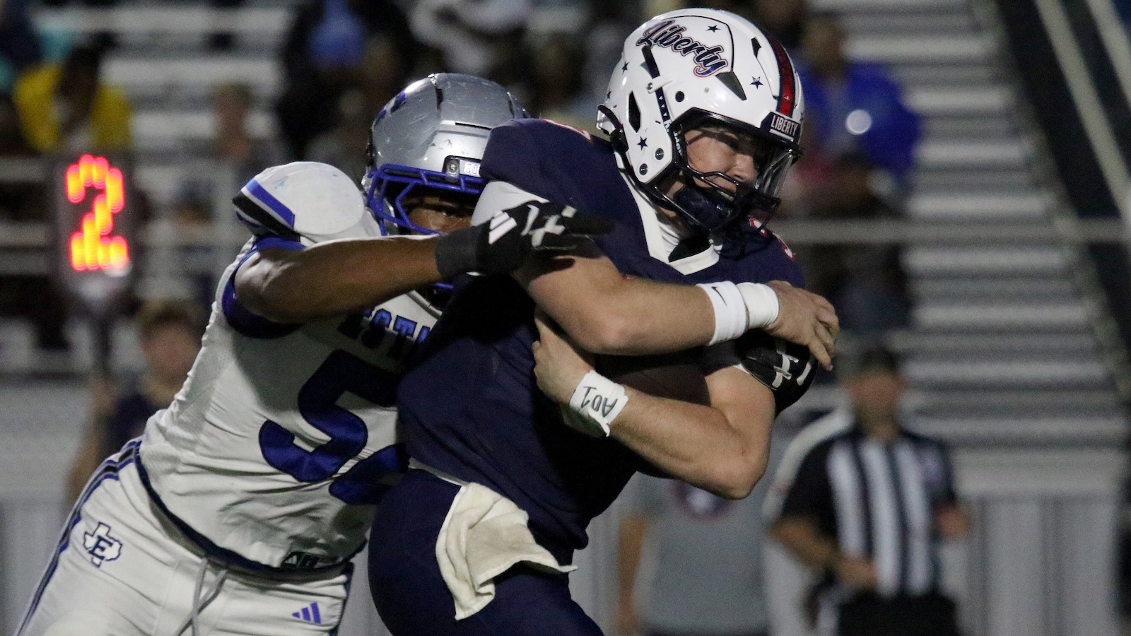 Two football players grapple during a tackle on the field, one in navy and one in white.