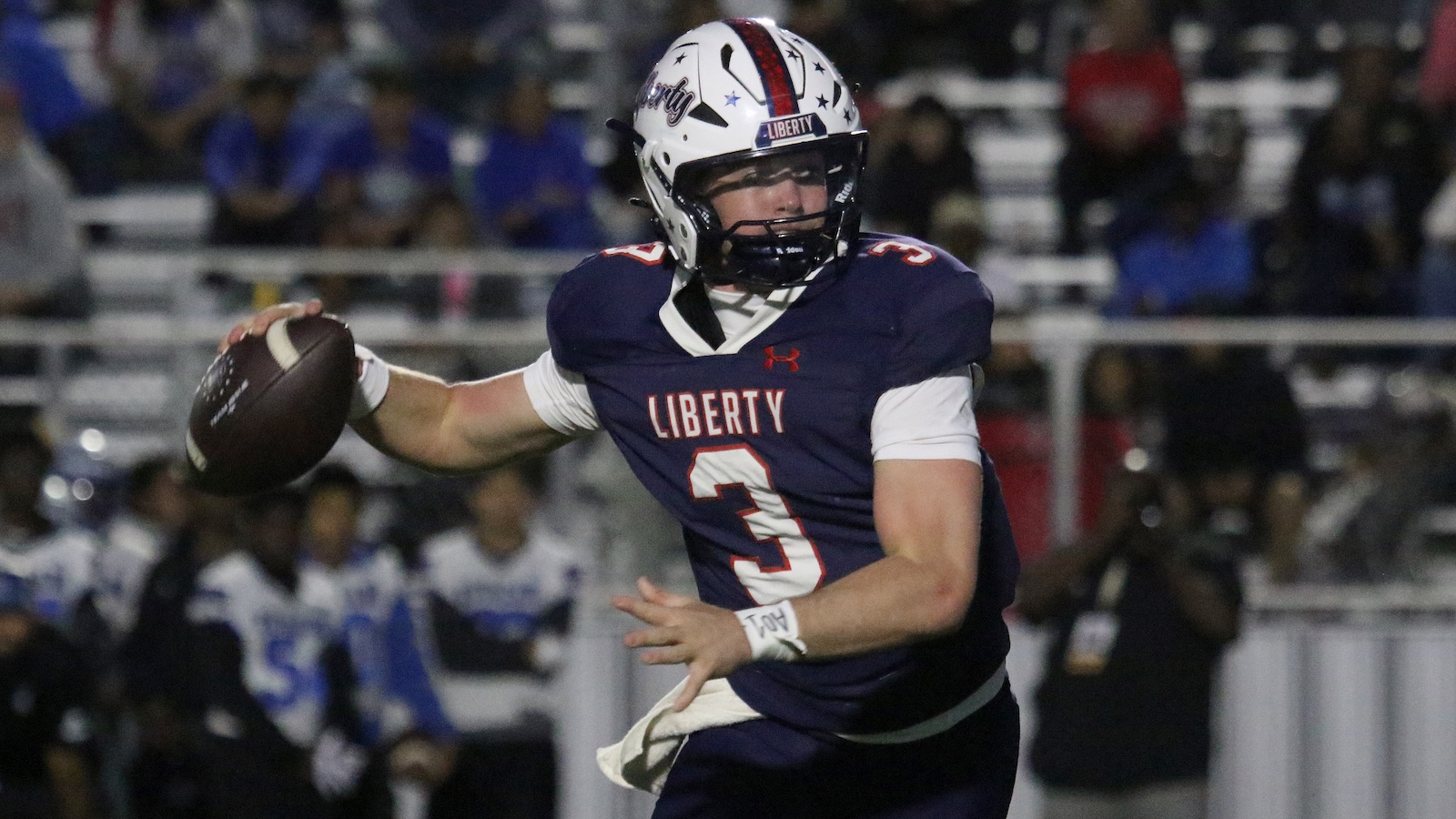 Liberty football quarterback (number 3) in dark navy uniform mid-throw with a football in hand on the field.
