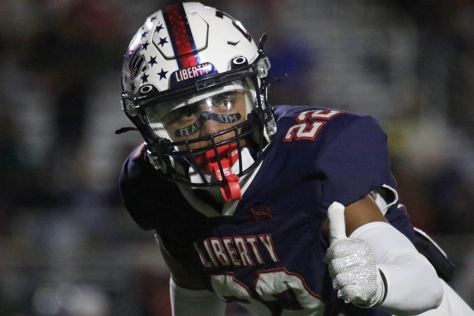 Liberty University football player in a navy jersey #25 charges forward, wearing a star-pattern helmet and red mouthguard.