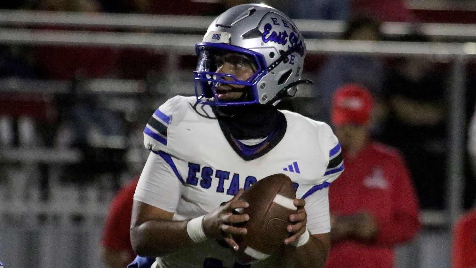 Football player in white and blue uniform cradling a football while looking to pass.