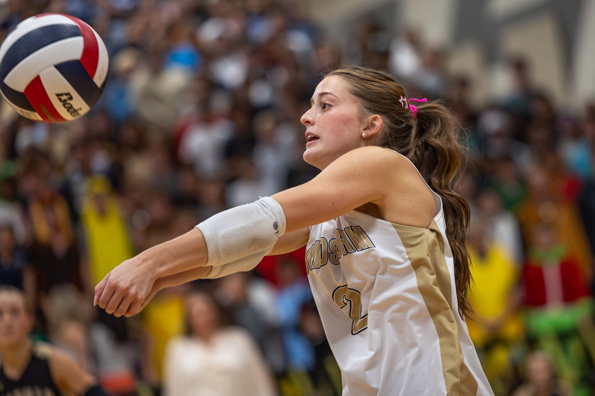 THS-AHS-VB-6 | Press Pass Sports Female volleyball player in white uniform extending arms to hit the ball, with a blurred crowd in the background.