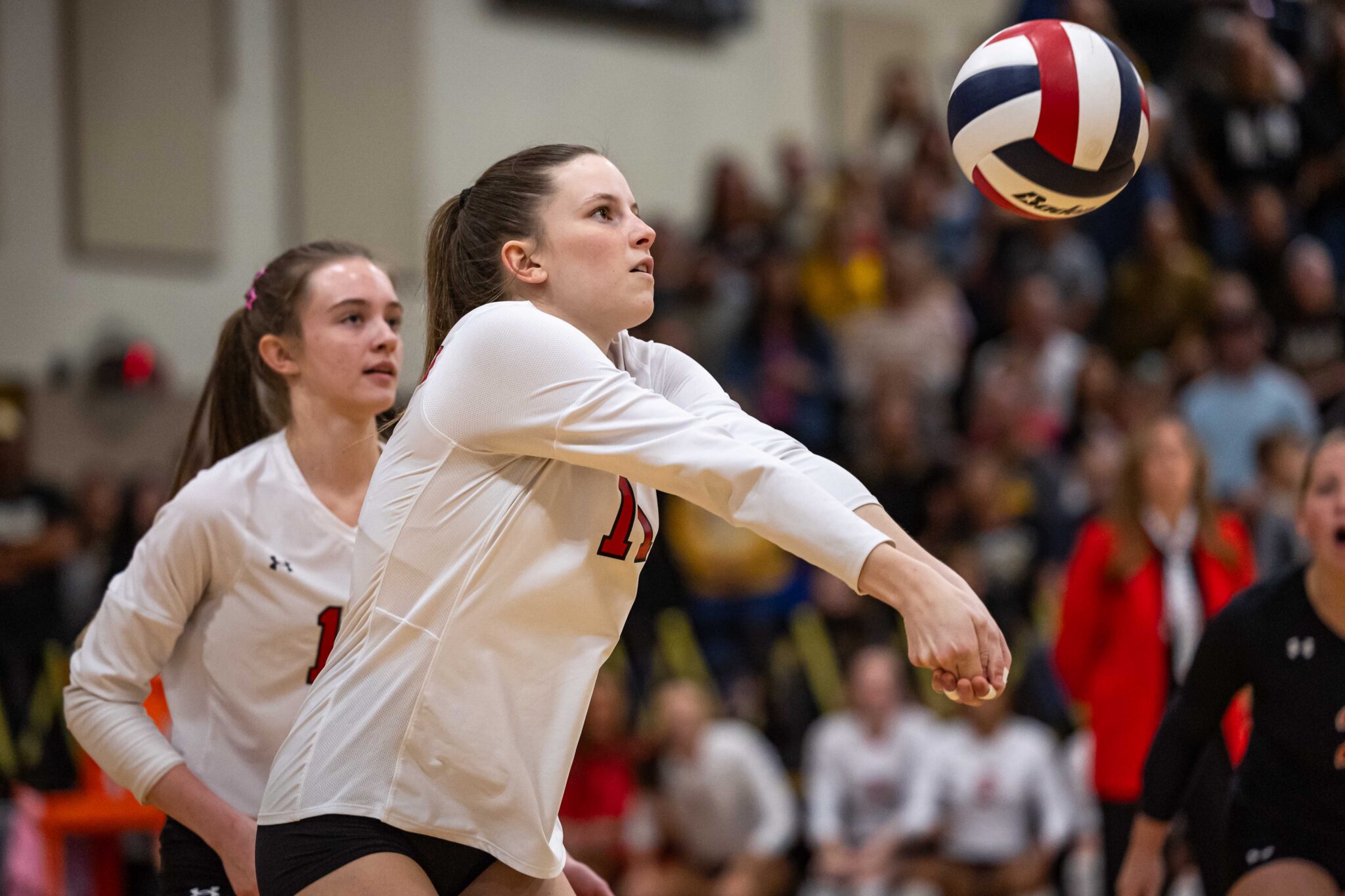 THS-AHS-VB-7 | Press Pass Sports Volleyball players in white jerseys dive toward a spinning ball in a crowded gym.
