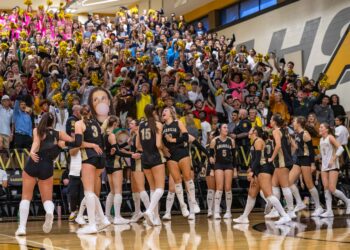 THS-AHS-VB-14 | Press Pass Sports Crowd of excited students in a gym cheering with gold pom-poms while basketball players in black uniforms stand in front on the court.
