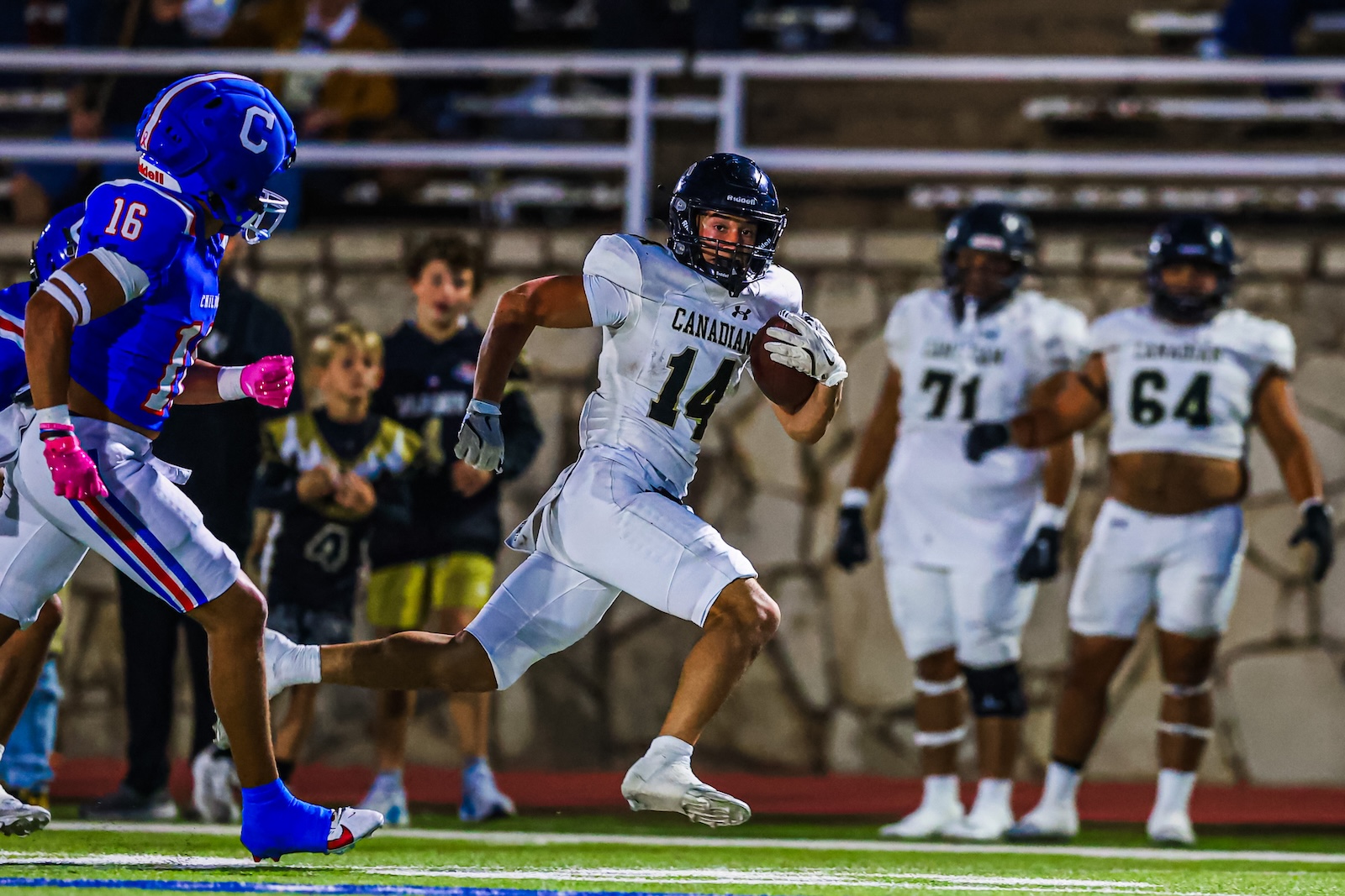 CT9A6848 | Press Pass Sports White Canadian football player sprints with the ball, number 14, pursued by a blue-team defender wearing number 16 on a football field.