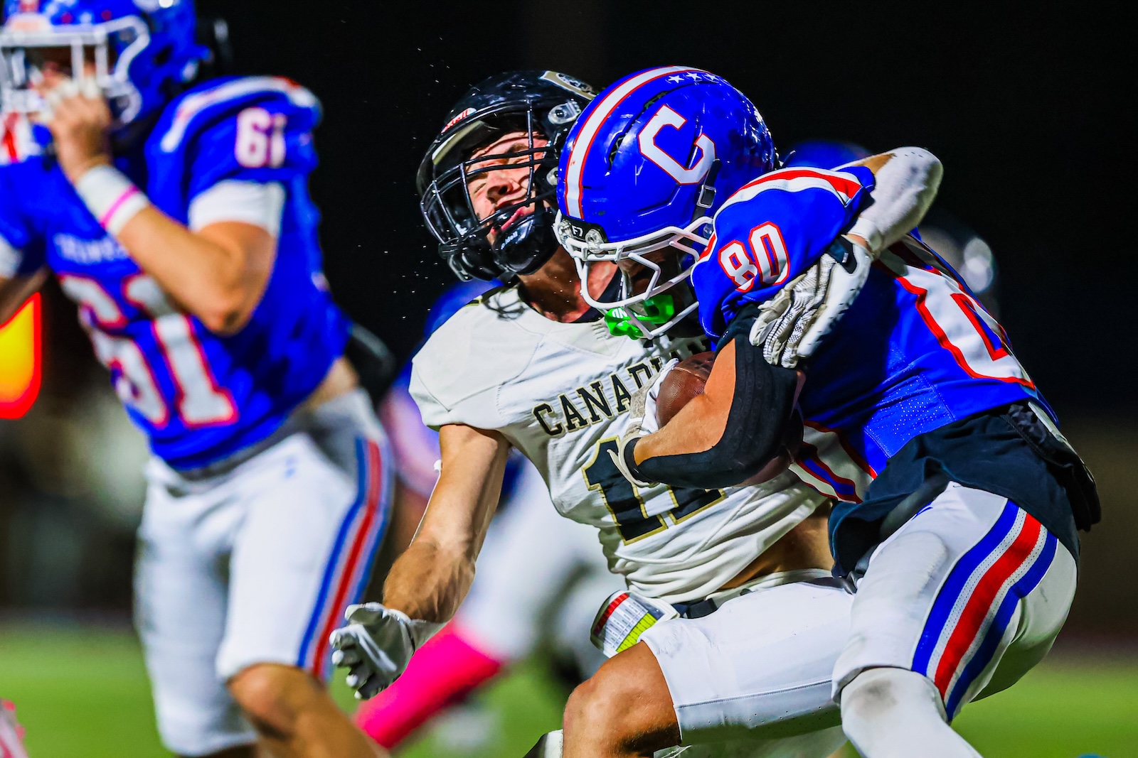 Canadian football player in white jersey (#11) is tackled by a defender in blue (#80) during a nighttime game under stadium lights.]?