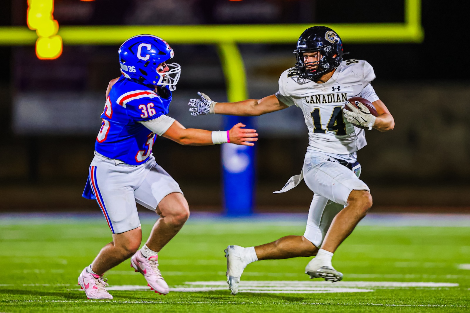 CT9A9636 | Press Pass Sports Two football players collide on a night game: blue jersey number 36 vs. white Canadian jersey number 14, rushing toward each other with ball carrier advancing.