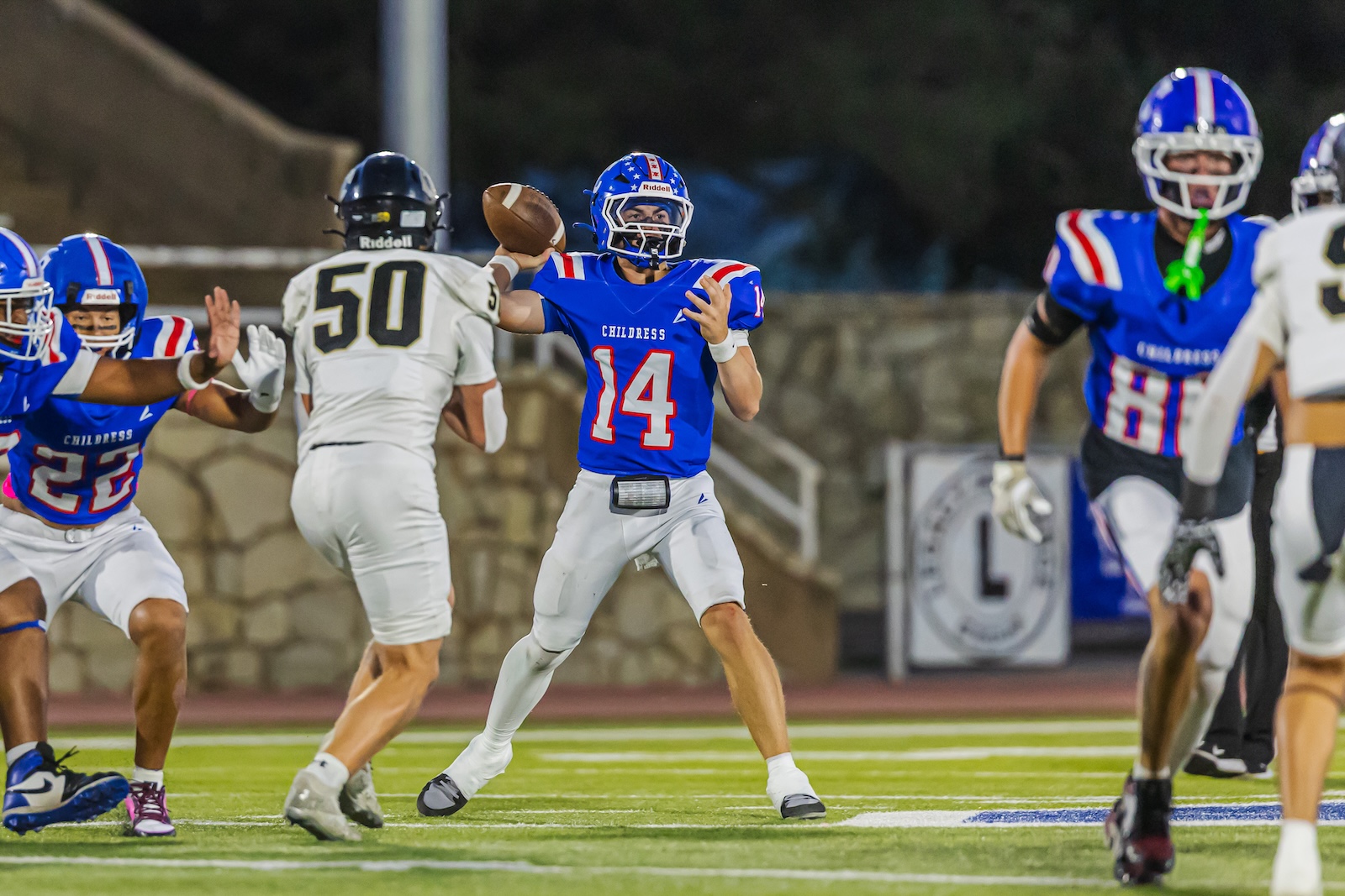 DE3_8598 | Press Pass Sports Blue team quarterback #14 throws a pass as defenders converge on the field.