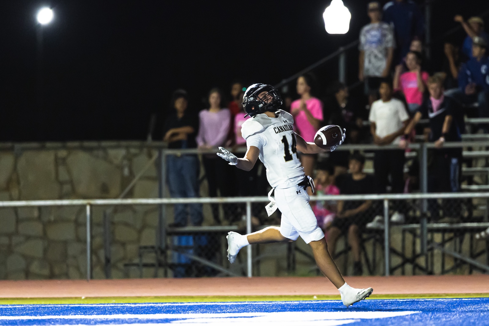 DE3_9788 | Press Pass Sports Football player in white jersey numbered 11 sprinting with the ball on blue turf at night, with spectators in the stands behind him.