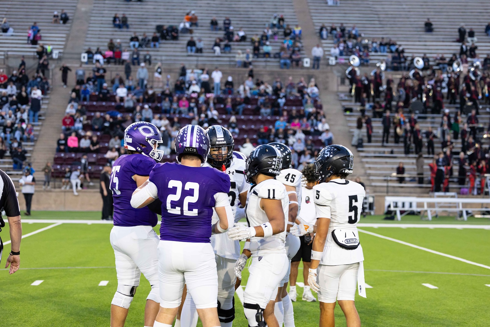 RHS-CHS-FB-2 | Press Pass Sports Football players in purple and white tops confront each other on a bright green field as crowds watch from the stands behind them.