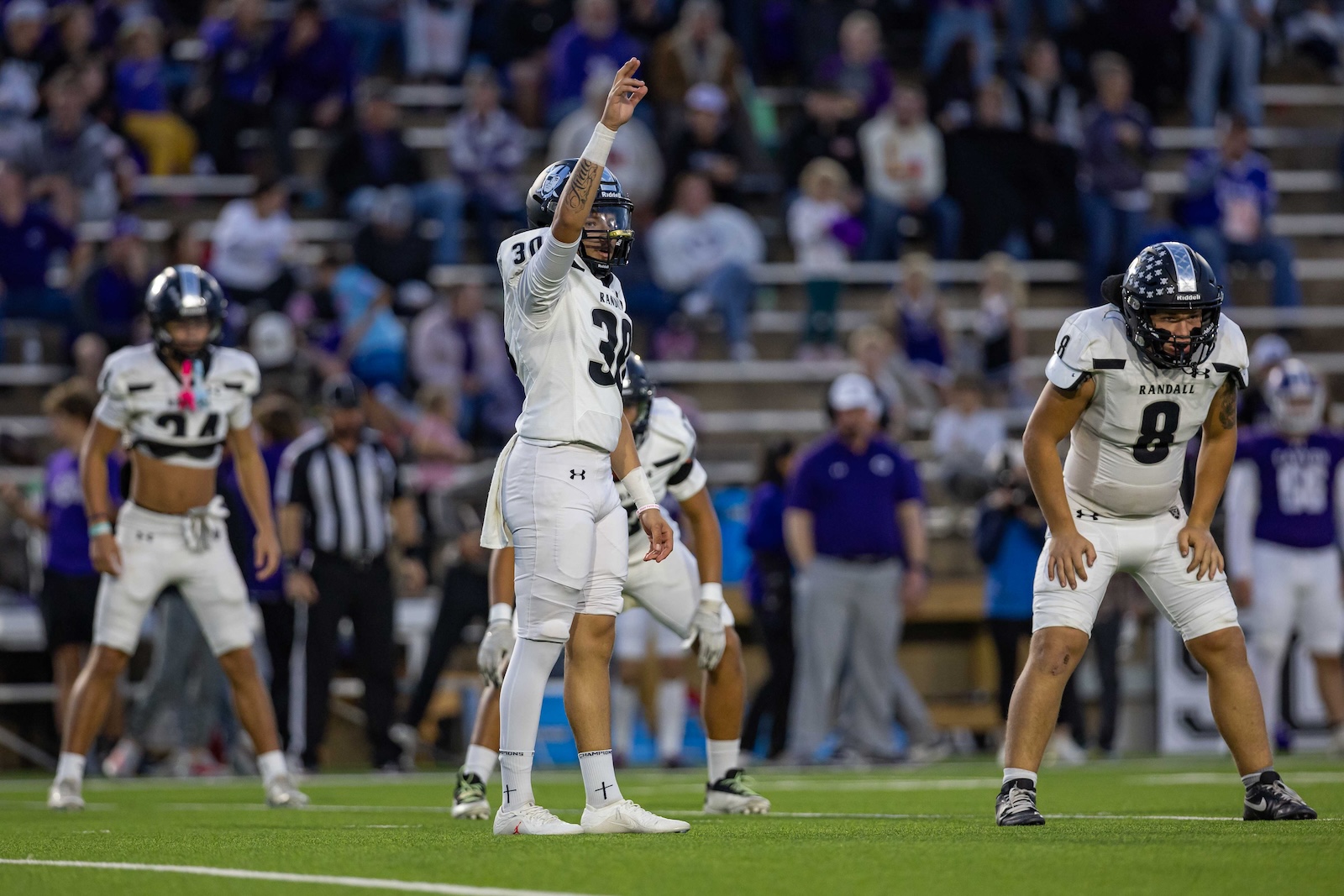 RHS-CHS-FB-4 | Press Pass Sports Football players in white uniforms on a green field; central player number 30 raises his arm as teammates and a crowd watch.