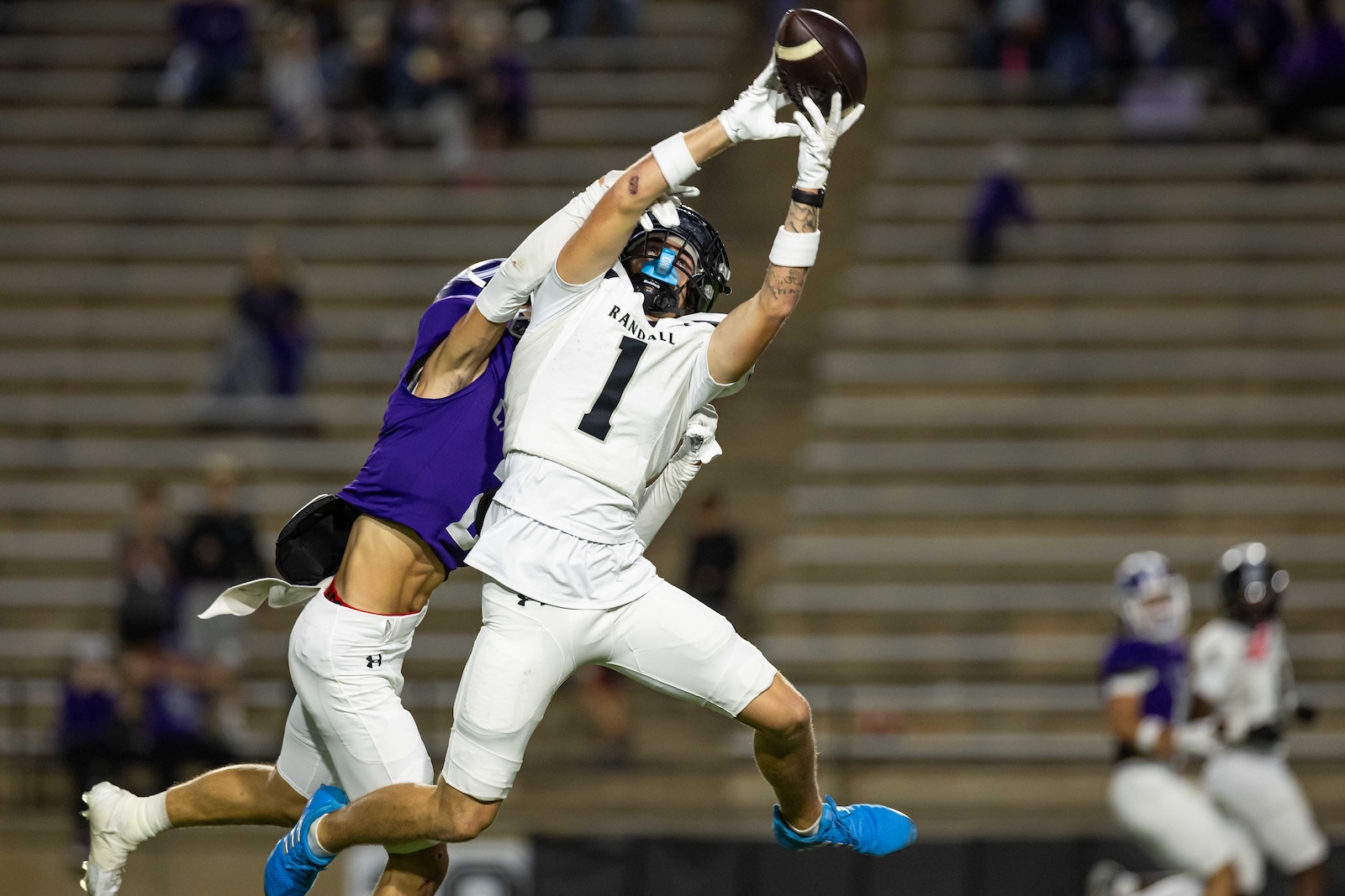 RHS-CHS-FB-11 | Press Pass Sports Two football players leap for a pass in midair: a white-jerseyed player wearing number 1 reaches for the ball while a purple-clad defender closes in.