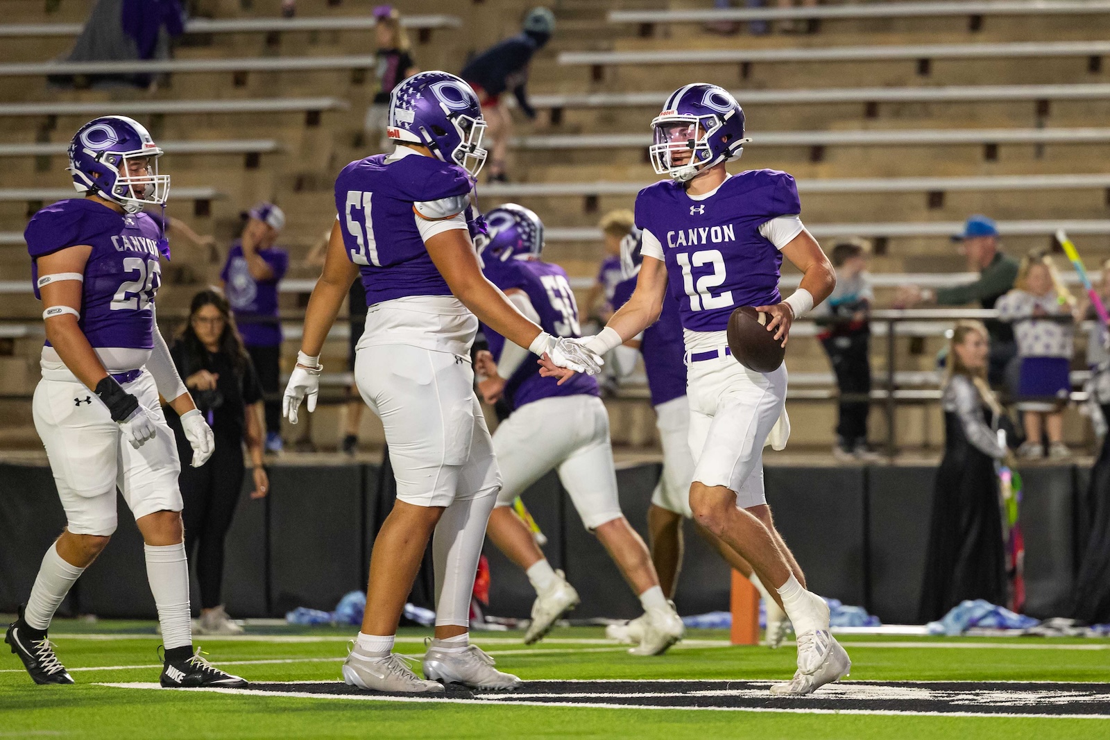 RHS-CHS-FB-17 | Press Pass Sports High school football players in purple uniforms high-fiving on the sideline, one holding a football.