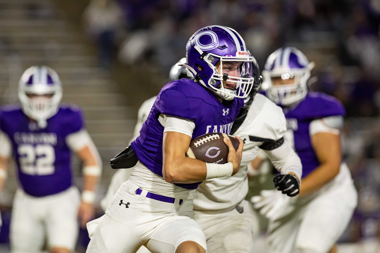 RHS-CHS-FB-21 | Press Pass Sports Football player in purple jersey and white pants runs with the ball during a game, defenders behind him.
