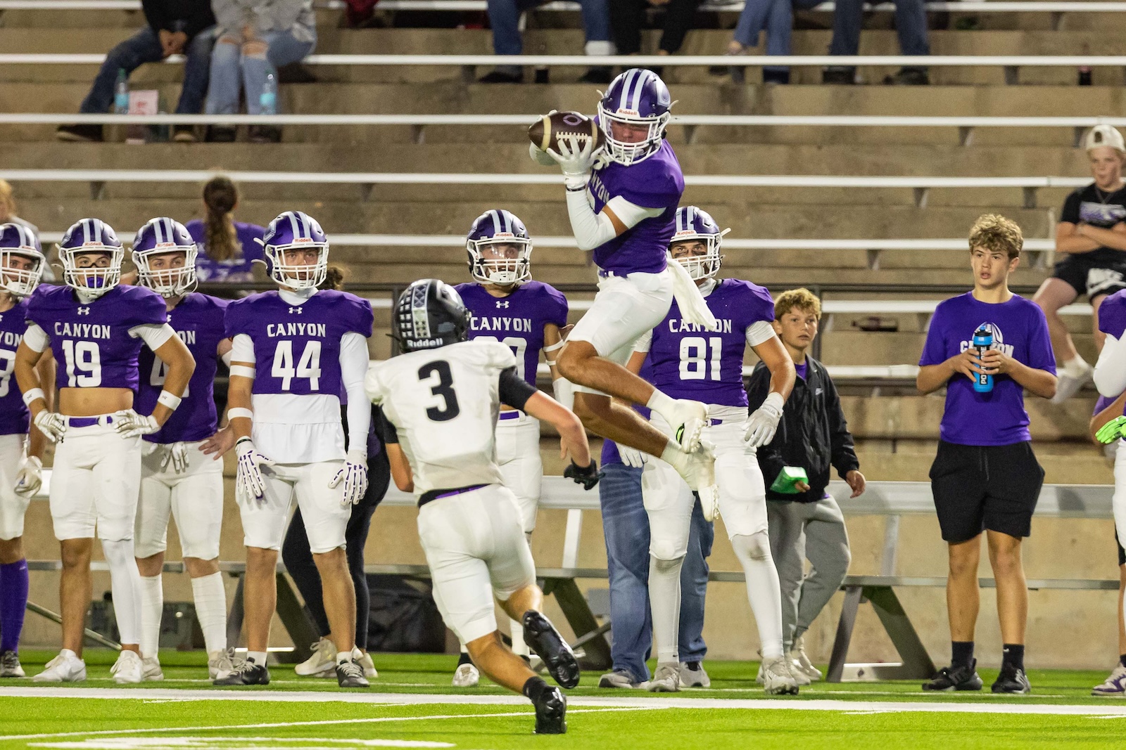 RHS-CHS-FB-22 | Press Pass Sports Football player in purple Canyon jersey leaps with ball for a catch as teammates watch from the sideline.