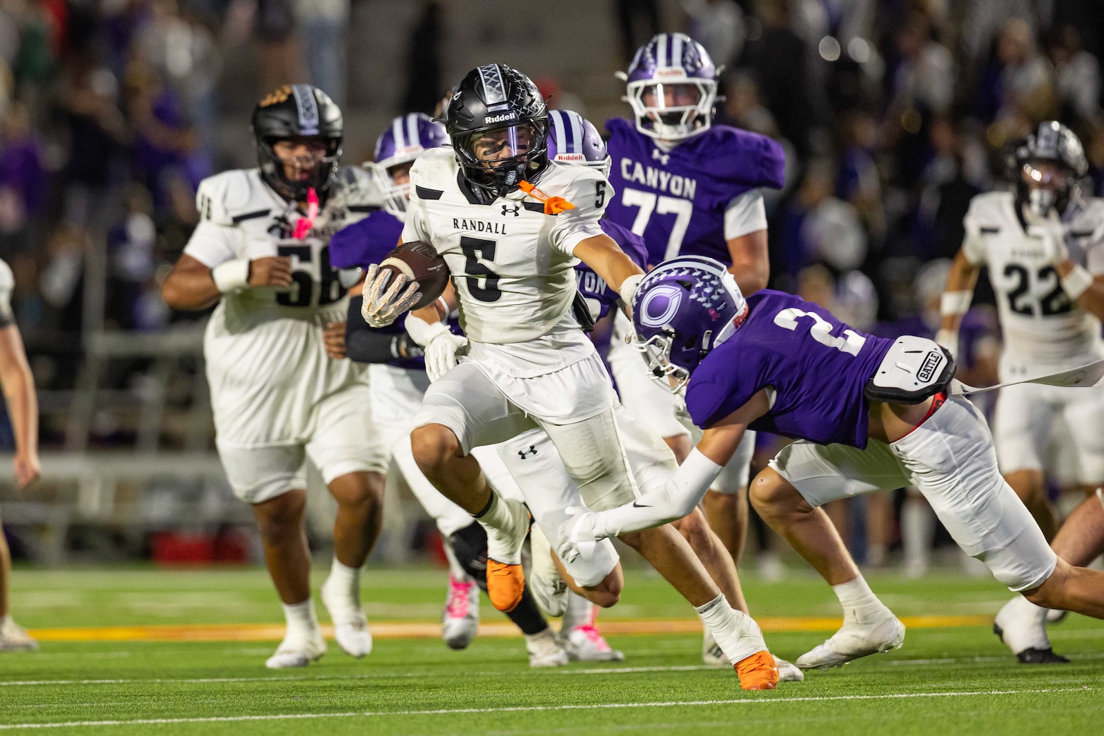 RHS-CHS-FB-29 | Press Pass Sports Randall #5 runs with the ball as purple-clad defenders chase him on a football field.