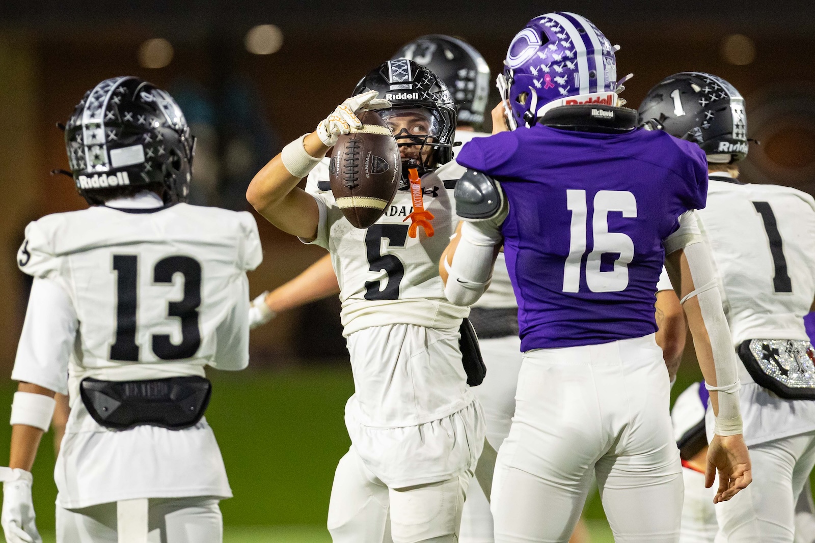RHS-CHS-FB-30 | Press Pass Sports White-uniform football players converge on the ball carrier wearing number 5, who holds a football toward the camera as teammates surround him; a purple-clad defender (#16) stands nearby.