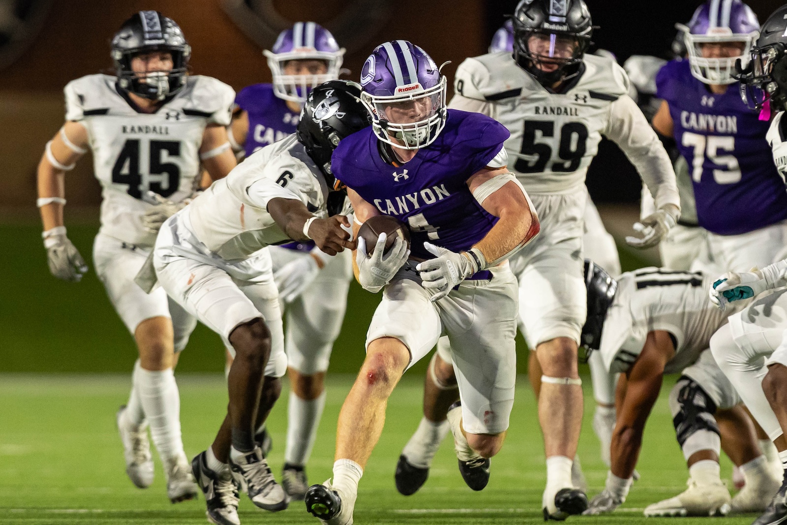 RHS-CHS-FB-34 | Press Pass Sports Canyon quarterback in purple jersey carries the ball, dodging white-clad defenders on a night football field.
