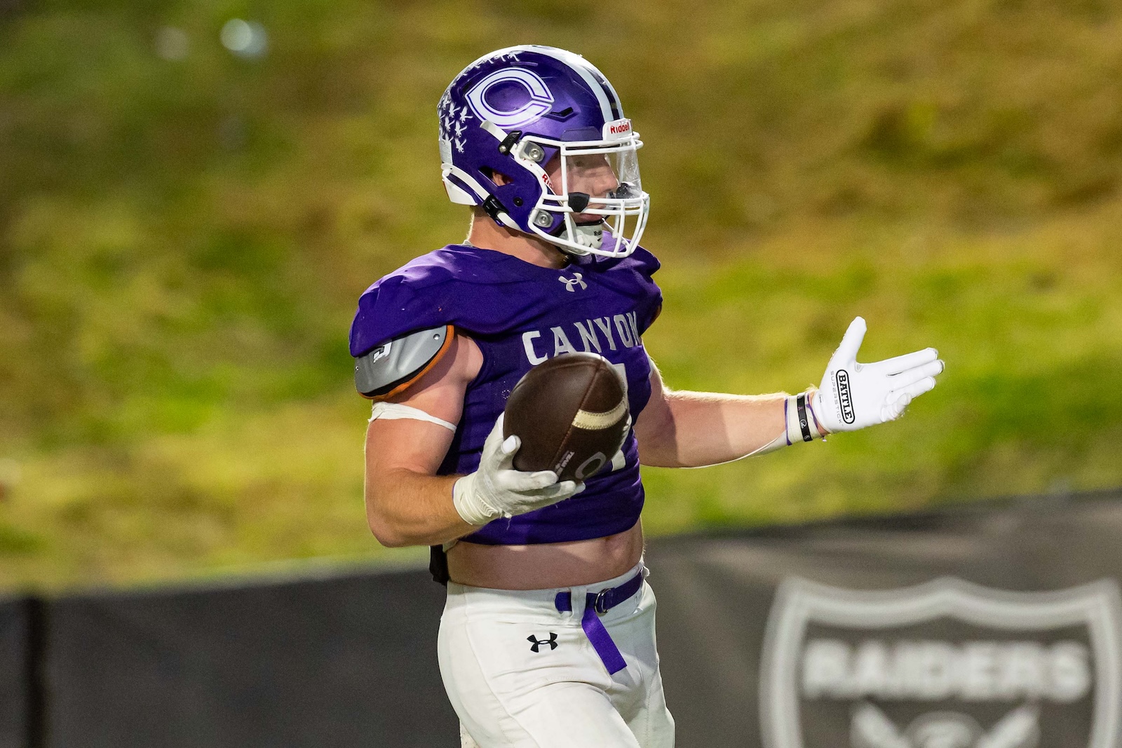 RHS-CHS-FB-35 | Press Pass Sports Football player in a purple Canyon jersey holding the ball while running on the field, helmet on and white gloves visible