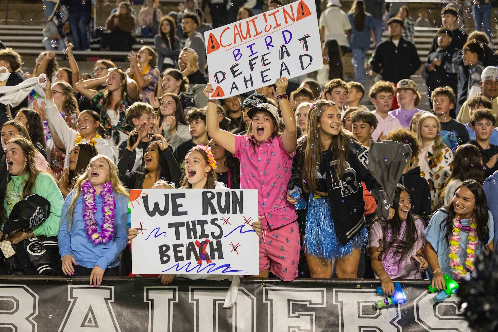 RHS-CHS-FB-37 | Press Pass Sports Crowd of cheering students at a stadium, holding signs like 'WE RUN THIS BEACH' and a large 'CAUTION: BIRD DEAD AHEAD' banner in the foreground.